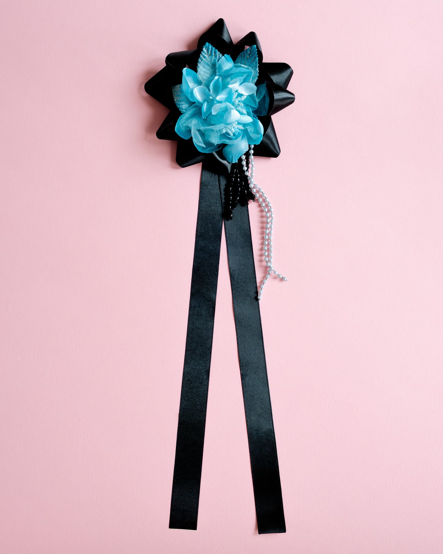 Black bow with blue flower and black ribbon on a pink background