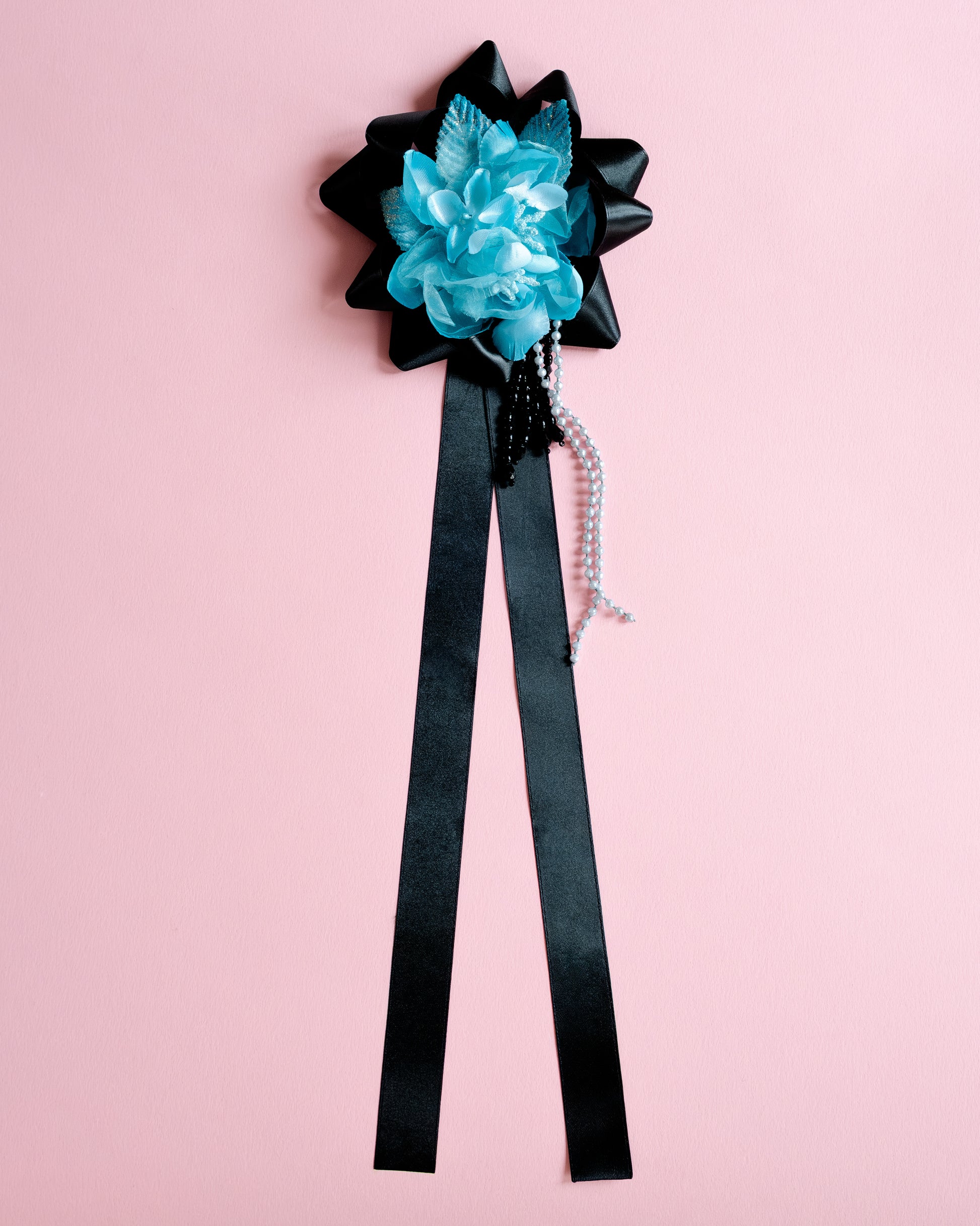 Black bow with blue flower and black ribbon on a pink background