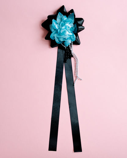 Black bow with blue flower and black ribbon on a pink background