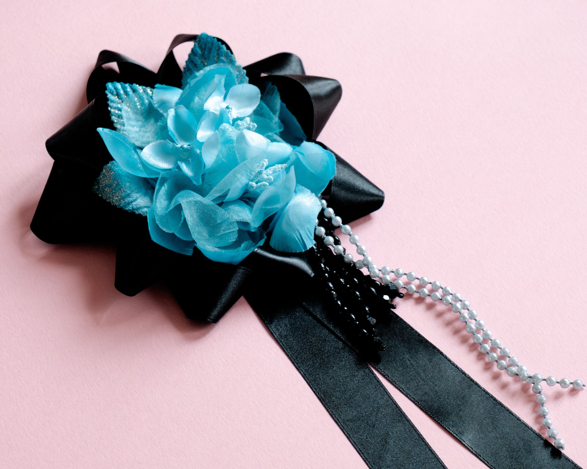 Blue flower corsage with black ribbon on a pink background